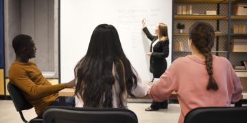 três alunos e uma professora na frente de um quadro explicando