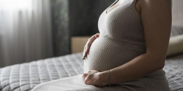 Pessoa grávida sentada com as mãos na barriga.